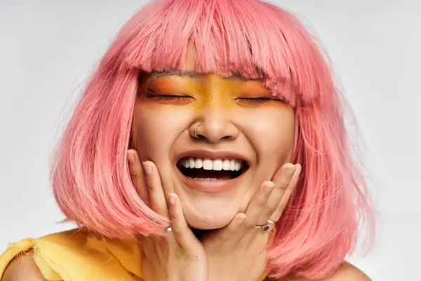 Una joven asiática con el pelo rosa exhibe alegremente su maquillaje artístico y estilo. - foto de stock