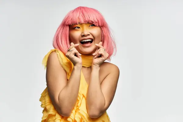 Uma jovem mulher asiática alegre em um vestido amarelo expressa alegria com gestos brincalhões. — Fotografia de Stock