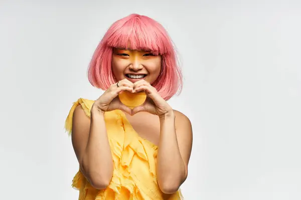 Brightly dressed young asian woman with pink hair joyfully forms a heart shape with her hands. — Stock Photo