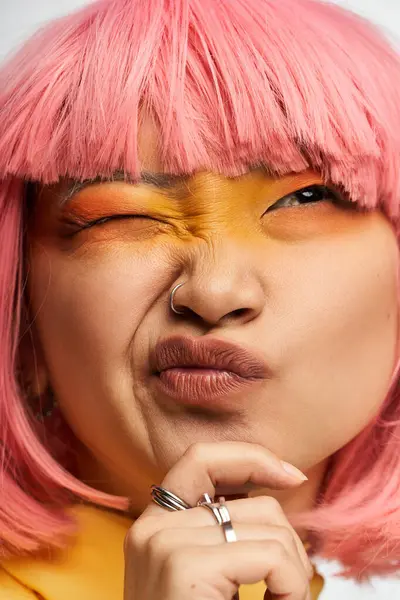 Una joven asiática con pelo rosa y maquillaje atrevido muestra juguetonamente su personalidad. - foto de stock