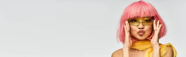 Mujer asiática joven con pelo rosa posa juguetonamente en gafas de sol con estilo sobre un telón de fondo neutral. - foto de stock