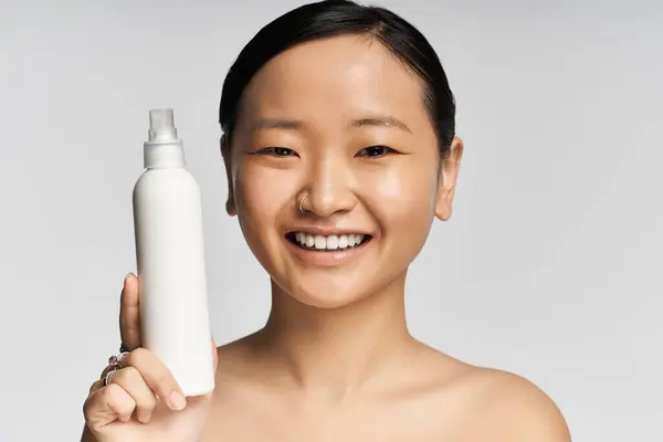 Smiling woman displays a skincare bottle while enjoying a bright and airy atmosphere. — Stock Photo