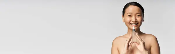 Young woman exudes joy and confidence as she showcases a skincare product in a minimalist setting — Stock Photo
