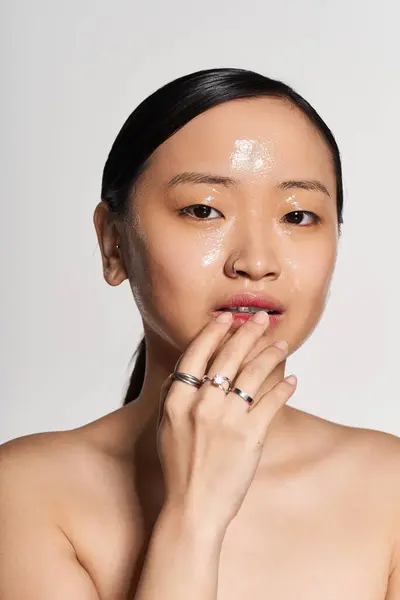 Una giovane donna asiatica si tocca delicatamente il viso, mostrando la sua pelle liscia e anelli alla moda. — Foto stock