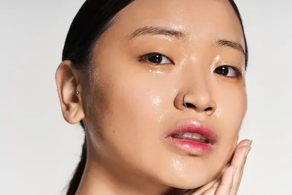 Una giovane bella donna asiatica tocca delicatamente il suo viso, irradiando fiducia e bellezza naturale. — Foto stock