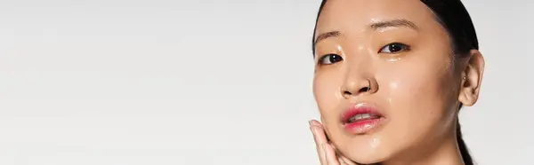 Radieuse jeune femme asiatique touche son visage, mettant en valeur son teint impeccable dans une scène de beauté. — Photo de stock