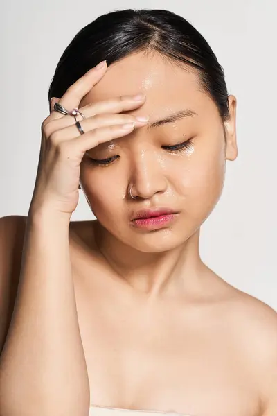 A young Asian woman thoughtfully touches her forehead against a simple artistic backdrop. — Stock Photo