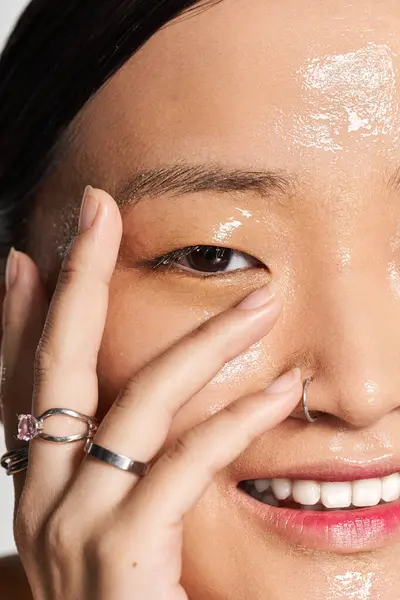 Una giovane donna asiatica applica un prodotto scintillante per la cura della pelle sorridendo gioiosamente nel suo spazio accogliente. — Foto stock