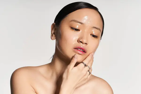 A young asian woman gently touches her cheek, showcasing radiant skin in soft natural light. — Stock Photo
