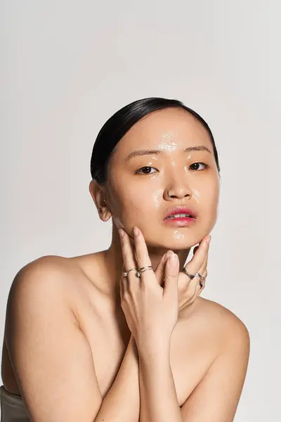 Une jeune femme asiatique applique des soins de la peau avec une expression sereine et une peau éclatante. — Photo de stock