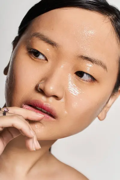A young Asian woman touches her face, showcasing her skincare routine and natural beauty. — Stock Photo