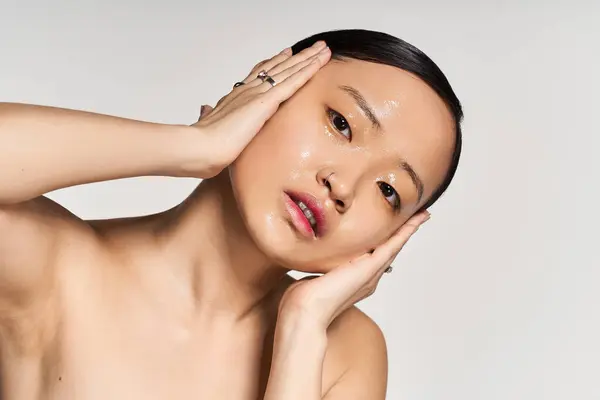 Giovane donna asiatica posa con le mani sul viso, mostrando la sua pelle rugiada in uno studio. — Foto stock