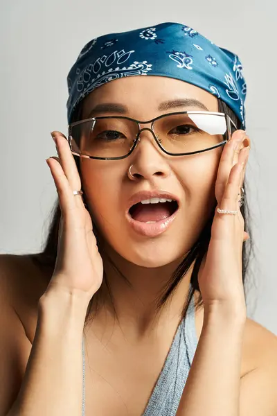 Una joven asiática alegre con gafas y un pañuelo azul posa en un elegante estudio. — Stock Photo