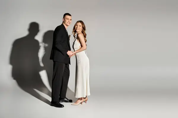 Beautiful bride and groom hold hands and smile, radiating love in a minimalist, elegant space. — Stock Photo
