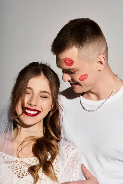 Joyful young bride beams as her groom smiles, sporting playful lipstick kisses on his forehead. — Stock Photo