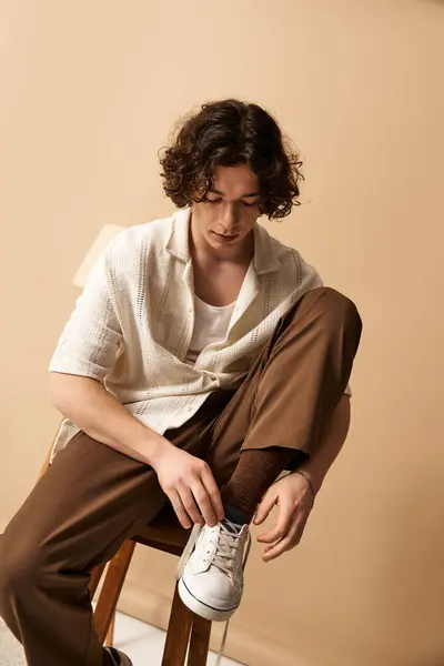A good looking young man with curly hair is adjusting his stylish shoes while seated in a studio. — Stock Photo