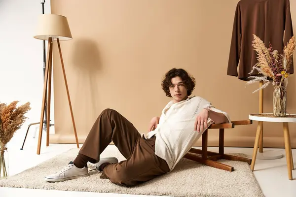 Un joven con el pelo rizado muestra un atuendo de verano de moda en un espacio de estudio minimalista. - foto de stock