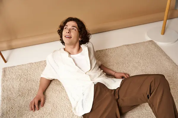 A young man with curly hair enjoys a relaxed moment in a stylish summer outfit in a studio. — Stock Photo