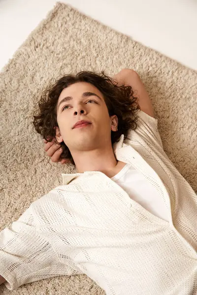 A young man relaxes on a plush rug, wearing a chic summer outfit that highlights his style. — Stock Photo