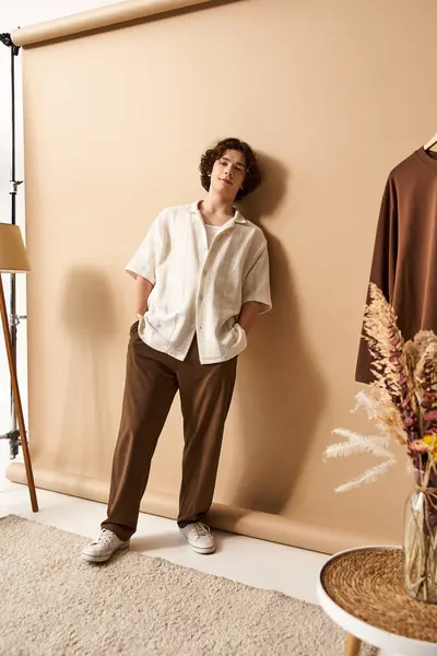 A young man with curly hair models a fashionable summer outfit while posing in a studio. — Stock Photo