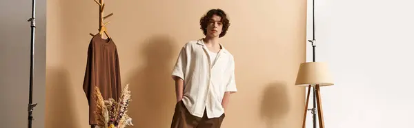 Joven guapo con el pelo rizado posa tranquilamente en un estudio moderno, usando atuendo de verano, pancarta - foto de stock