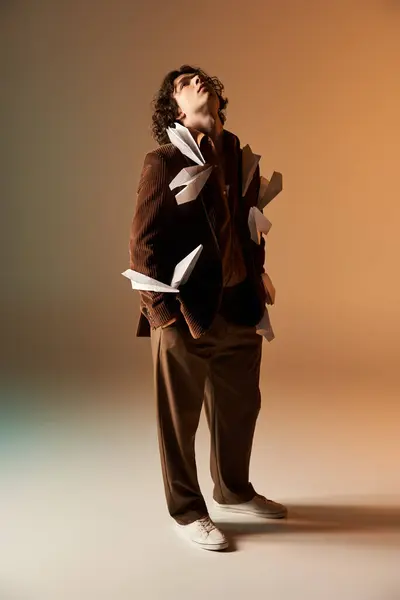 Young man with curly hair models a brown corduroy blazer adorned with paper planes in a studio. — Stock Photo