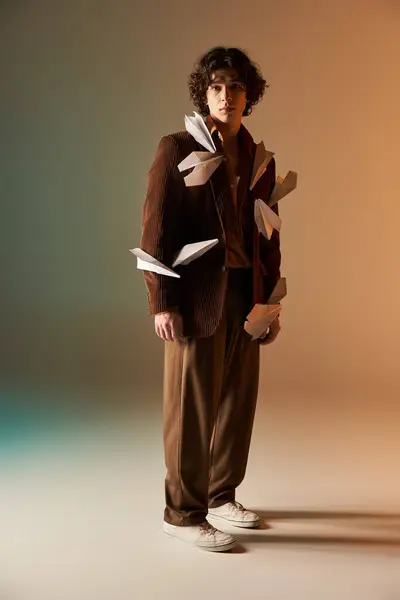 A stylish young man with curly hair sports a trendy outfit featuring paper planes. — Stock Photo