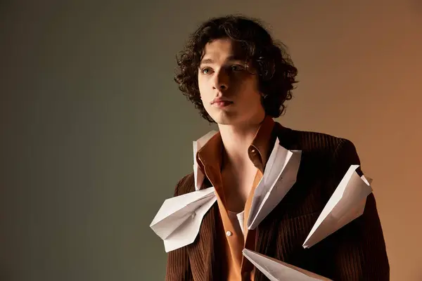 Young man in a brown corduroy blazer expresses creativity with paper planes in a studio. — Stock Photo