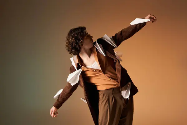 Stylish young man with curly hair confidently shows off paper planes on his blazer in a studio. — Stock Photo