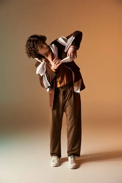A stylish young man playfully interacts with paper planes on his brown blazer in the studio. — Stock Photo