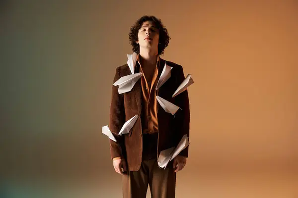 A confident young man with curly hair poses amid paper planes and a creative backdrop. — Stock Photo