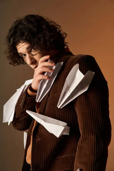 A young man with curly hair poses confidently in a brown corduroy blazer adorned with paper planes. — Stock Photo