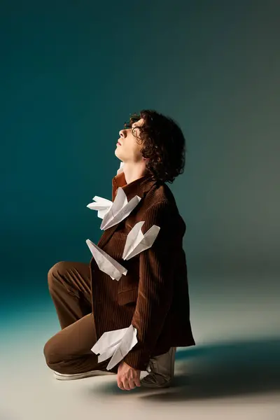 Curly-haired man in a brown corduroy blazer poses creatively with paper planes, showcasing artistry. — Stock Photo