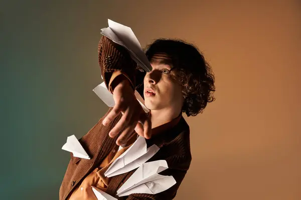 Curly-haired young man poses in a brown corduroy blazer as paper planes float around him. — Stock Photo