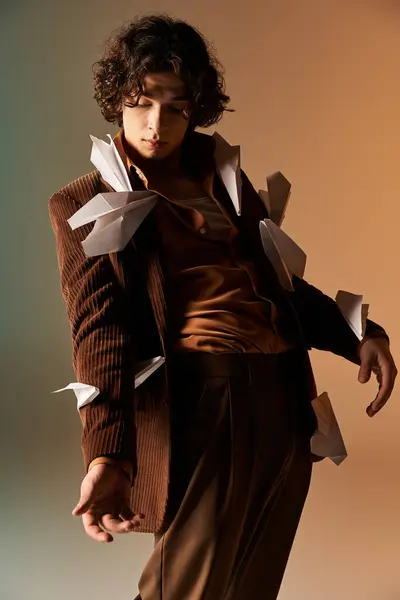 A young man with curly hair poses stylishly in a studio, adorned with paper planes. — Stock Photo