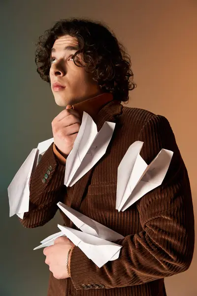 A young man with curly hair poses confidently in a brown corduroy blazer, adorned with paper planes. — Stock Photo