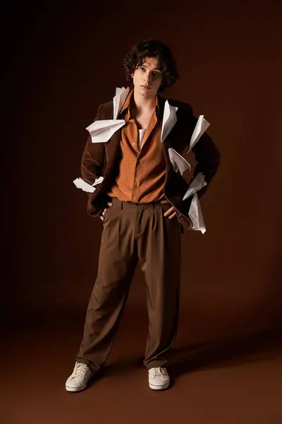 A good looking young man with curly hair poses in a stylish outfit featuring paper planes decor. — Stock Photo