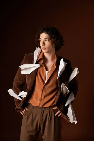 A young man with curly hair showcases his stylish brown corduroy blazer adorned with paper planes. — Stock Photo