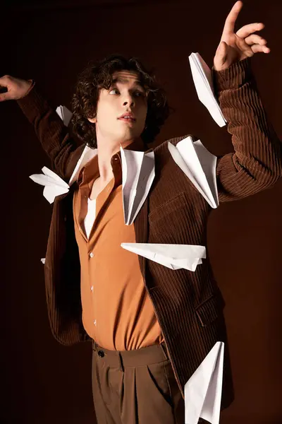 A curly-haired young man shows off his stylish outfit and playful energy with paper planes. — Stock Photo