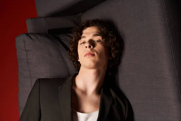 A good looking young man with curly hair relaxes against a textured backdrop, exuding style. — Stock Photo