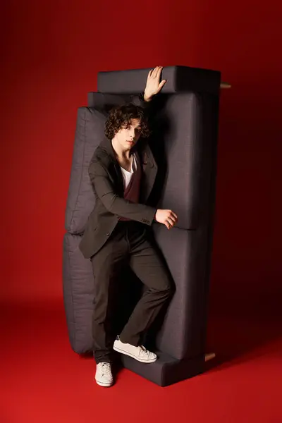 A young man with curly hair showcases a modern black outfit against a striking red backdrop. — Stock Photo