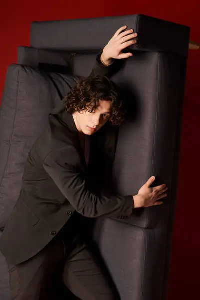 A young man with curly hair poses in fashionable black clothing, exuding confidence. — Stock Photo