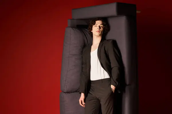 Good looking young man with curly hair showcases a chic black outfit in a studio environment. — Stock Photo