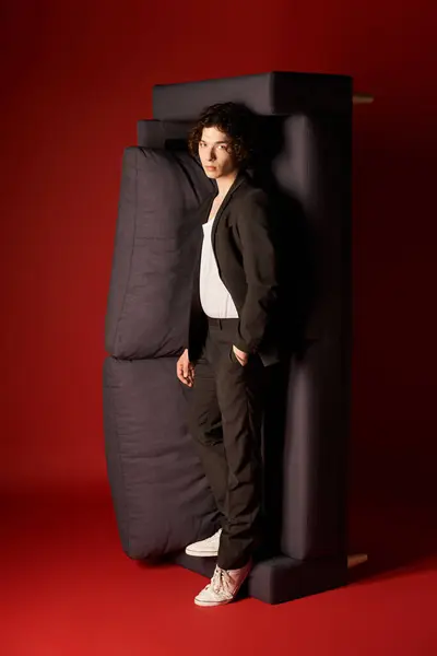 A stylish young man in sleek black attire stands confidently against a bold red backdrop. — Stock Photo