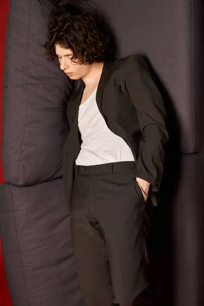Jovem de cabelos encaracolados em uma roupa preta elegante fica confiante, capturando a atenção em um estúdio. — Fotografia de Stock