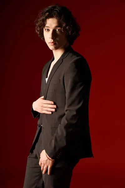 Um jovem em traje preto elegante confiantemente está contra um cenário de estúdio vibrante. — Fotografia de Stock