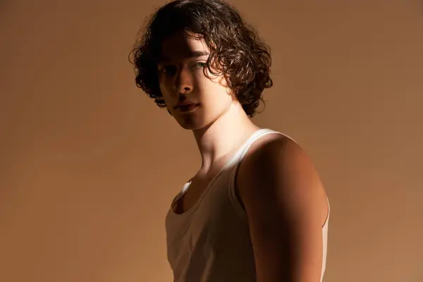Ein gut aussehender junger Mann mit lockigem Haar präsentiert sein stylisches Tanktop in einem kreativen Atelier. — Stockfoto