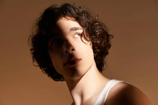 A young man with curly hair captivates with his stylish presence in a studio setting. — Stock Photo