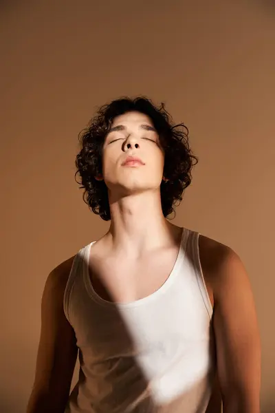 Stylish young man with curly hair stands confidently in a studio, embracing the light. — Stock Photo