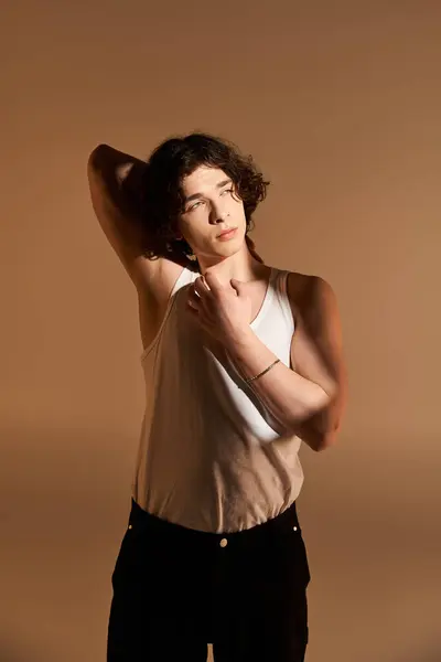 Young man with curly hair poses confidently in a tank top against a warm studio backdrop. — Stock Photo